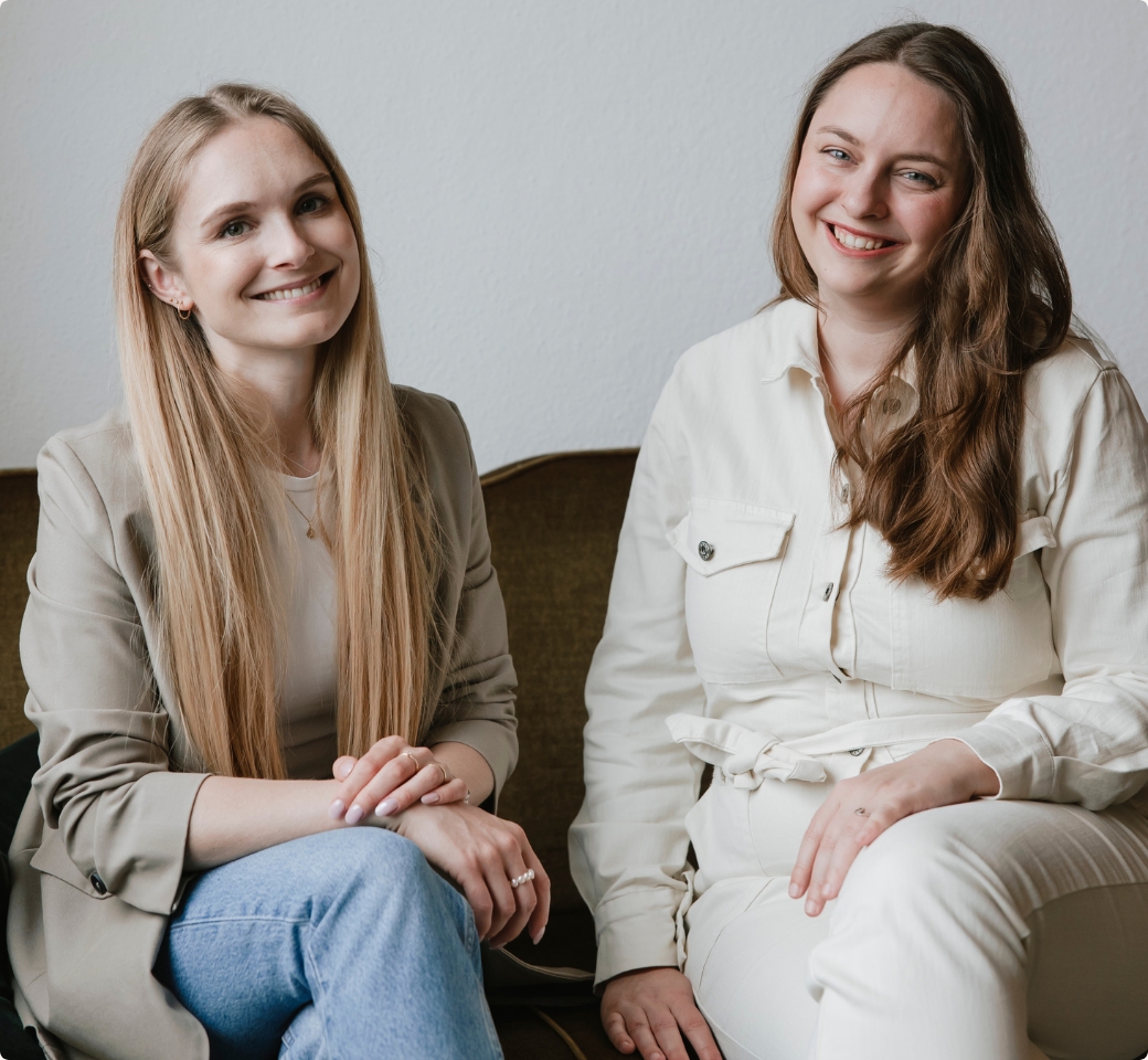 Nathalie sitzt in einem Café am Laptop und laechelt in die Kamera