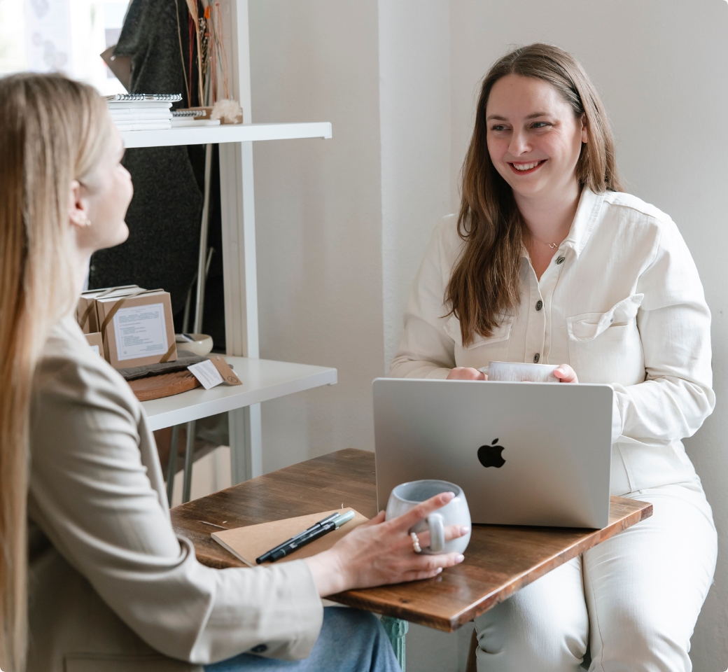 Nathalie sitzt in einem Café am Laptop und laechelt in die Kamera